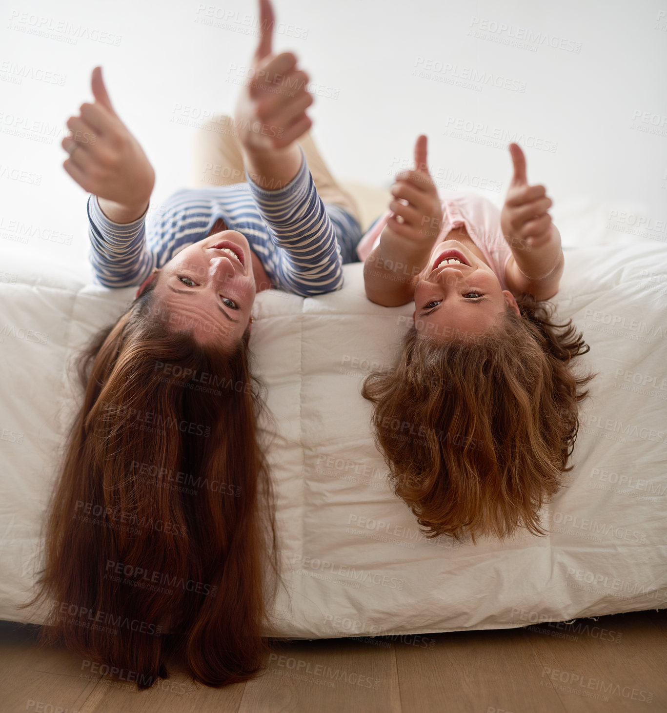 Buy stock photo Shot of a mother and her daughter hanging uspide down off the edge of a bed
