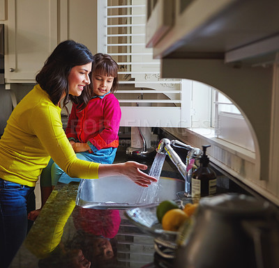 Buy stock photo Shot of a young mother and her daughter running water in the kitchen sink