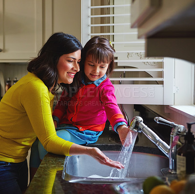 Buy stock photo Shot of a young mother and her daughter running water in the kitchen sink