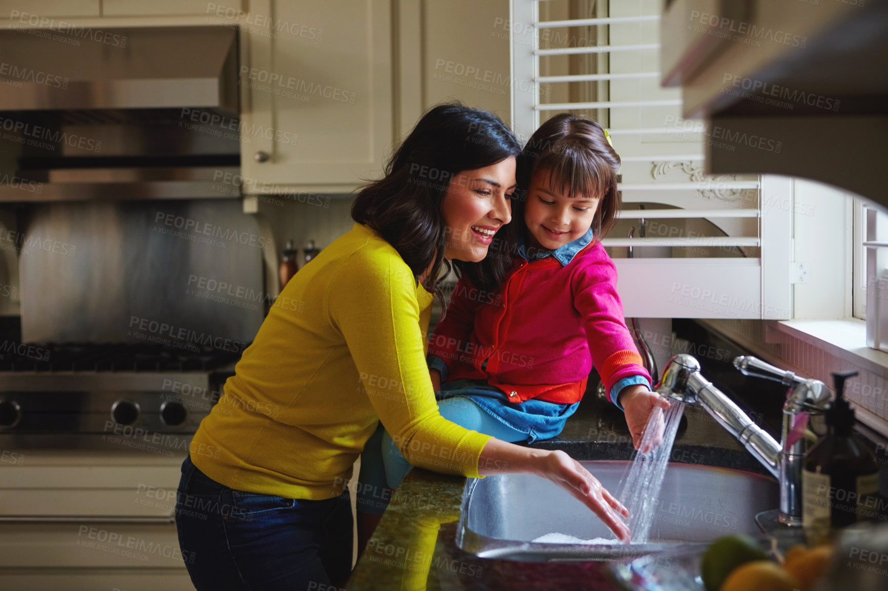 Buy stock photo Shot of a young mother and her daughter running water in the kitchen sink