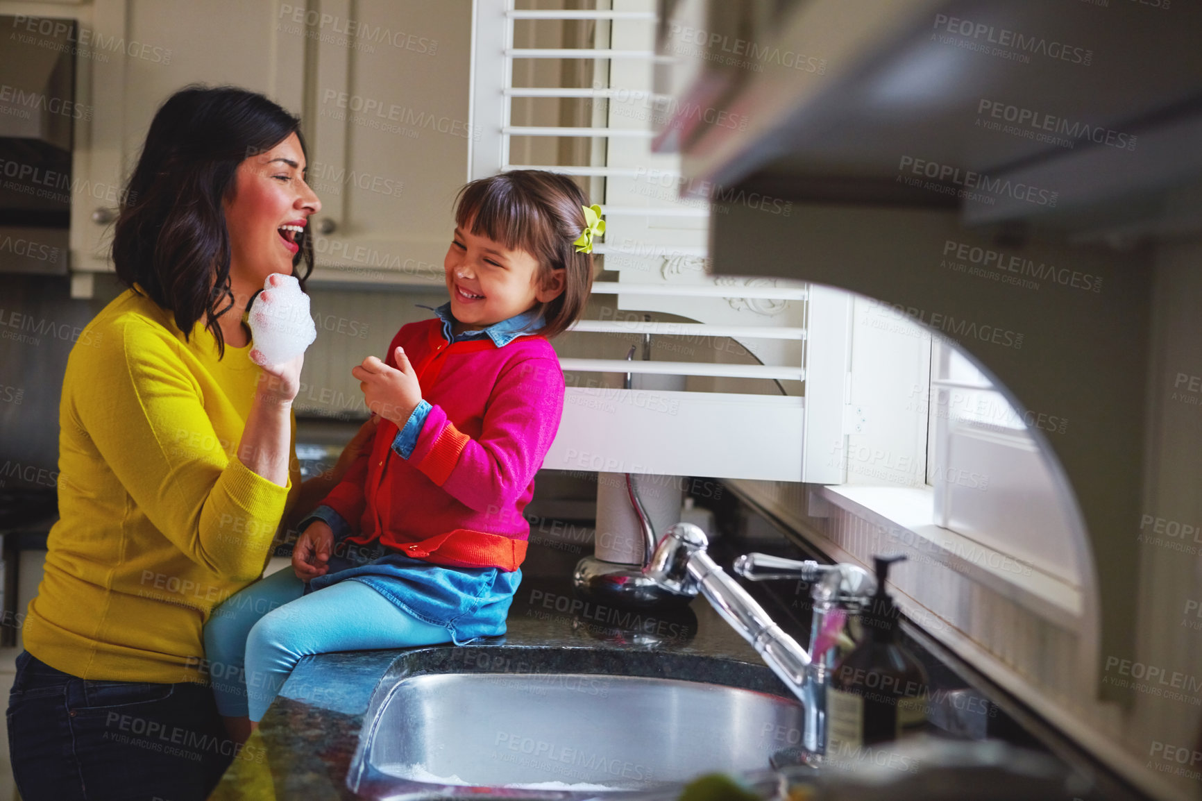 Buy stock photo Shot of a young mother and her daughter playing by the kitchen sink