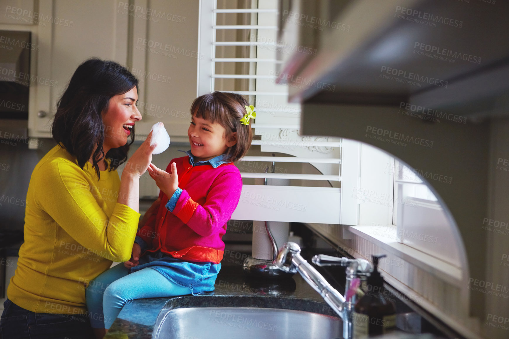 Buy stock photo Shot of a young mother and her daughter playing by the kitchen sink