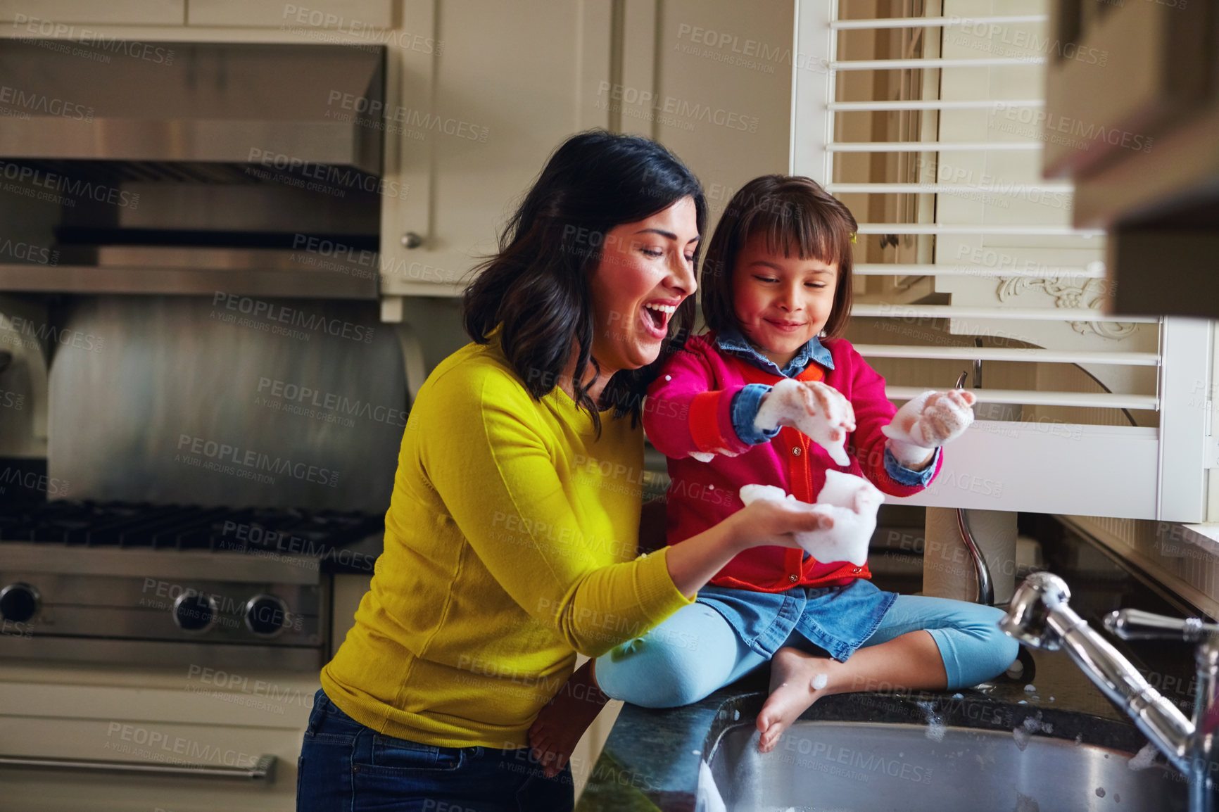 Buy stock photo Shot of a young mother and her daughter playing by the kitchen sink