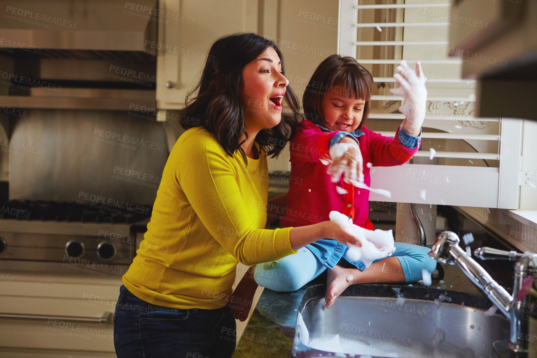 Buy stock photo Shot of a young mother and her daughter playing by the kitchen sink