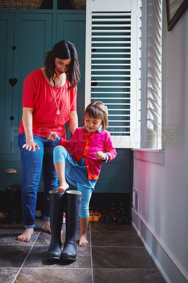 Buy stock photo Full length shot of a mother helping her daughter try on a pair of large rain boots at home