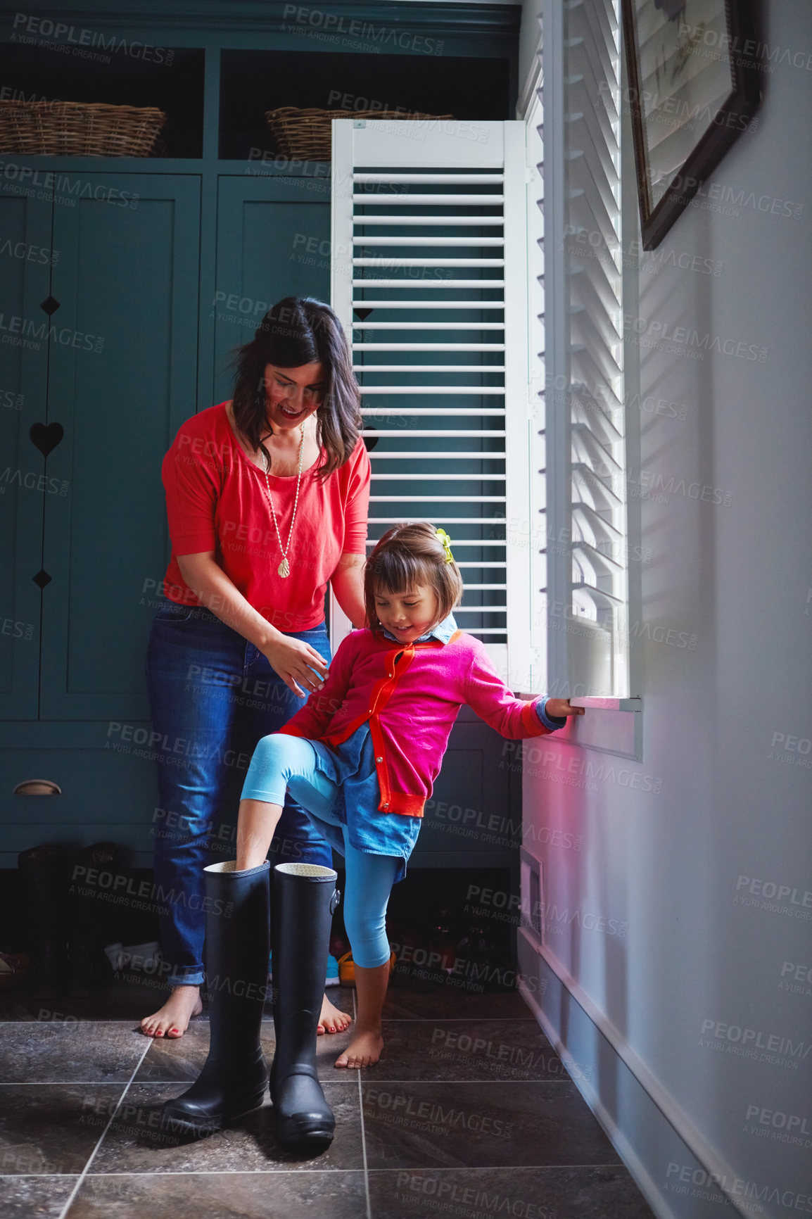 Buy stock photo Full length shot of a mother helping her daughter try on a pair of large rain boots at home