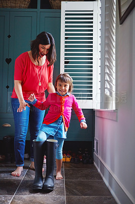 Buy stock photo Full length shot of a mother helping her daughter try on a pair of large rain boots at home