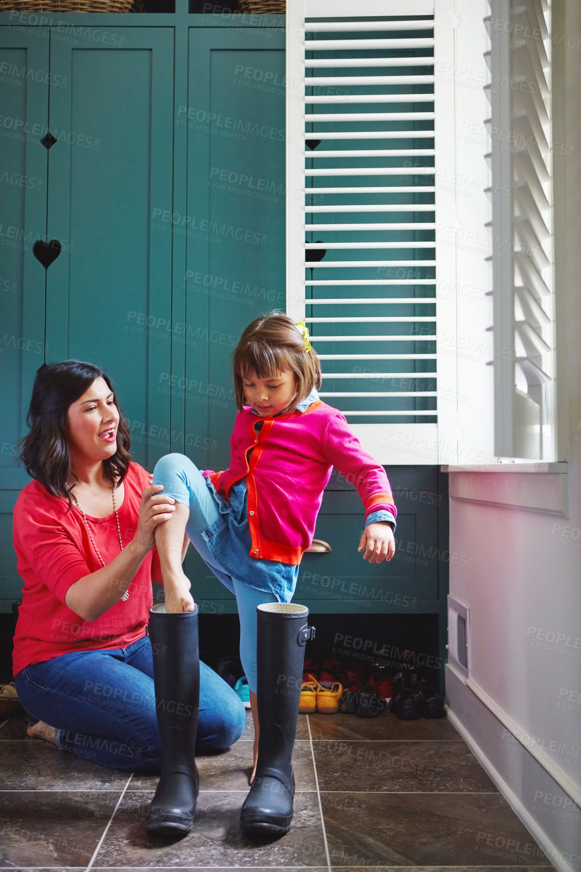 Buy stock photo Full length shot of a mother helping her daughter try on a pair of large rain boots at home