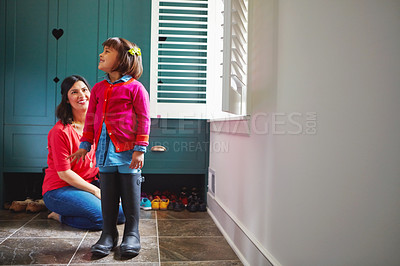 Buy stock photo Full length shot of a mother watching her daughter try on a pair of large rain boots at home