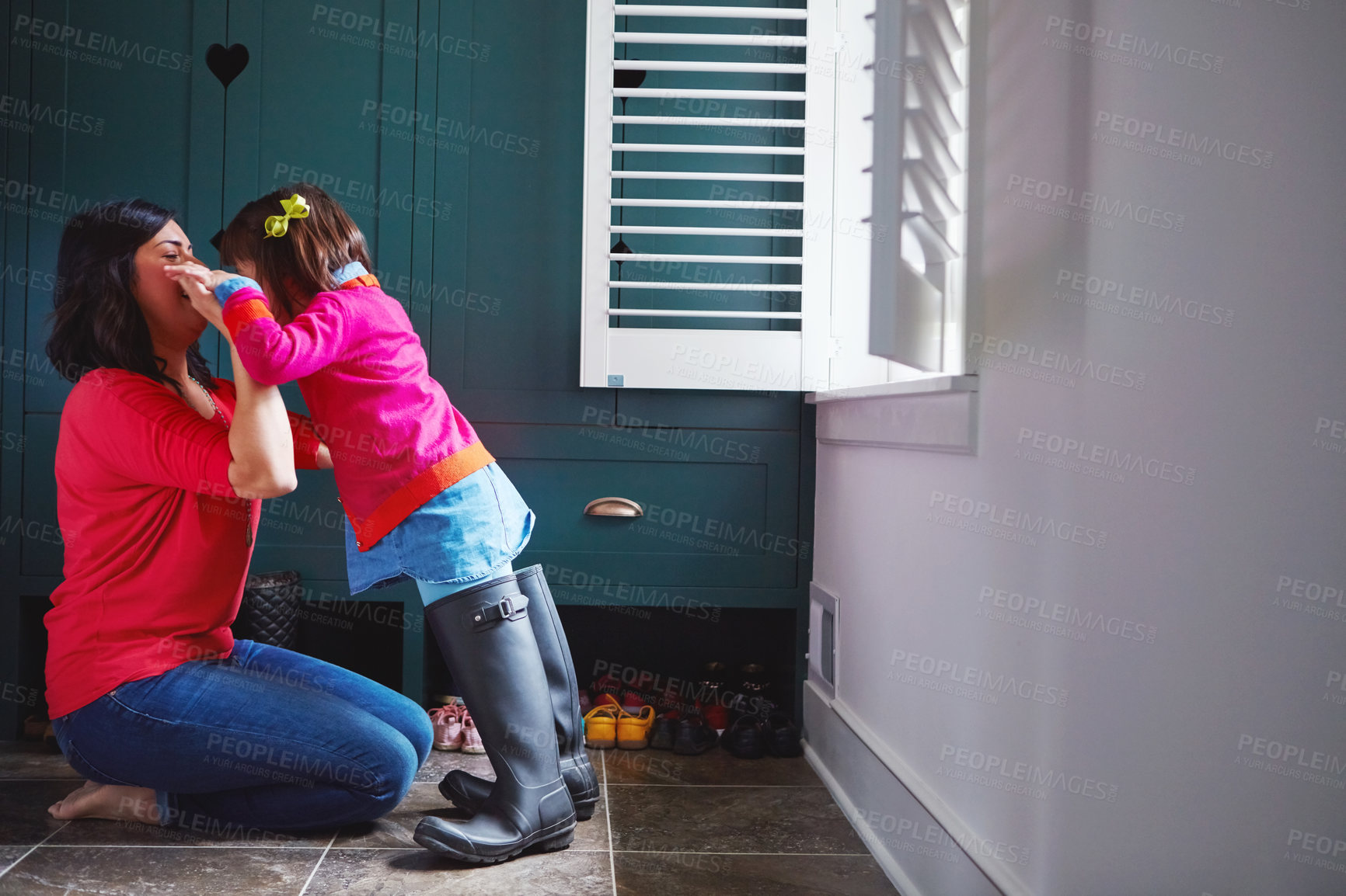 Buy stock photo Full length shot of a mother helping her daughter try on a pair of large rain boots at home