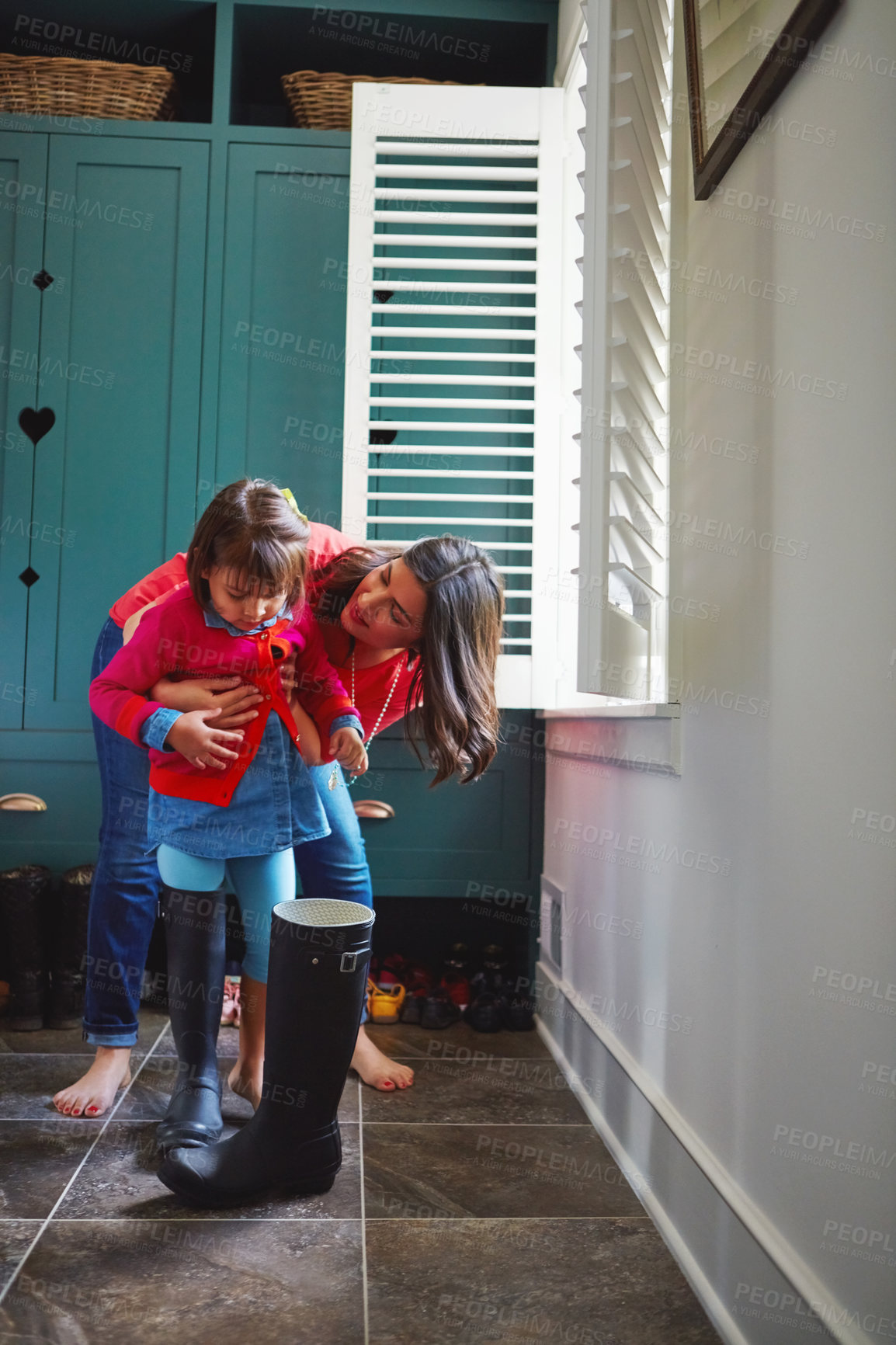 Buy stock photo Full length shot of a mother helping her daughter try on a pair of large rain boots at home