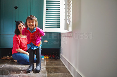 Buy stock photo Full length shot of a mother watching her daughter try on a pair of large rain boots at home