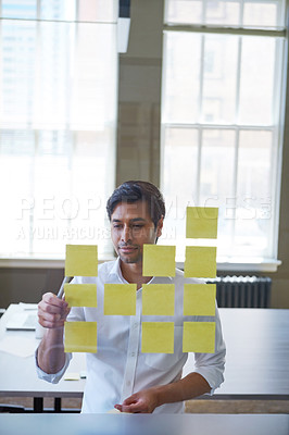 Buy stock photo Cropped shot of a handsome businessman arranging adhesive notes on a glass pane