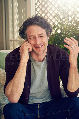 Buy stock photo Cropped shot of a man sitting and talking on his cellphone outside his home