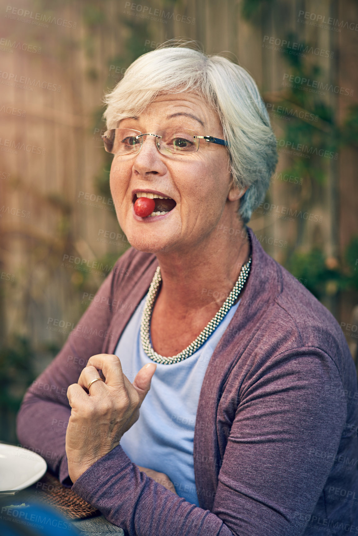 Buy stock photo Senior woman, eating tomato and lunch outdoor with smile, glasses and meal for Christmas celebration. Elderly person, hungry and fruit with food in summer, happy or relax at festive event in backyard
