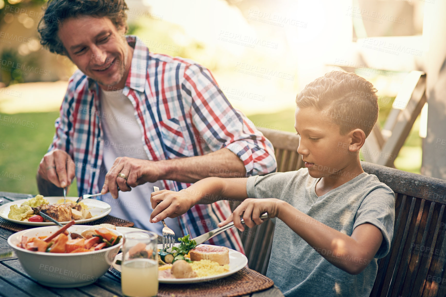 Buy stock photo Smile, dad and child at outdoor lunch on patio for thanksgiving, family event and eating together in backyard. Care, father and son at table for garden picnic with food, happy bonding and support