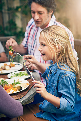 Buy stock photo Shot of a happy little girl enjoying an outdoor lunch with her family