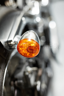 Buy stock photo The side indicator light of a motorbike. Closeup of signal gleam with the rear turning indicator light of a parked motorcycle. Popup of a rear signal glare with a chrome finish and orange LED light