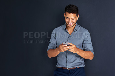 Buy stock photo Studio shot of a young businessman texting on a cellphone against a dark background