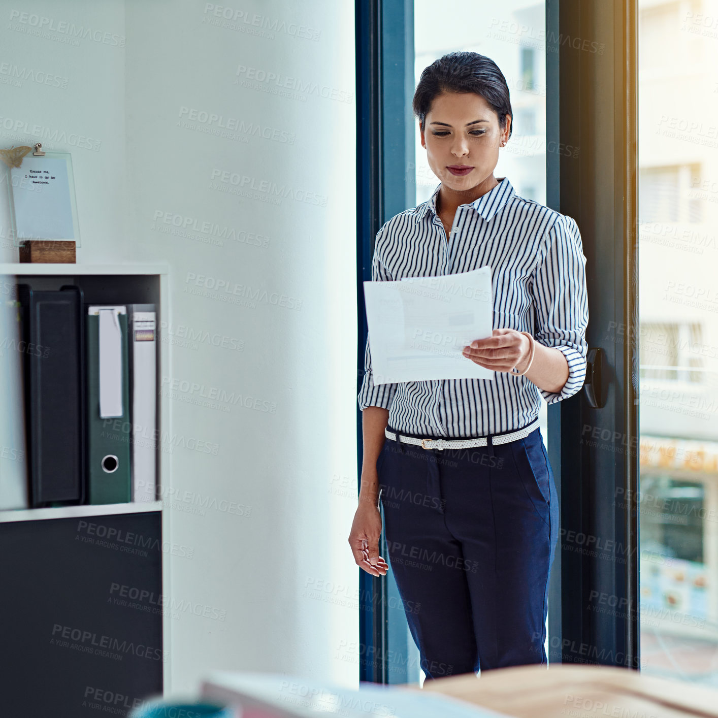 Buy stock photo Shot of a young businesswoman looking through some paperwork in an office