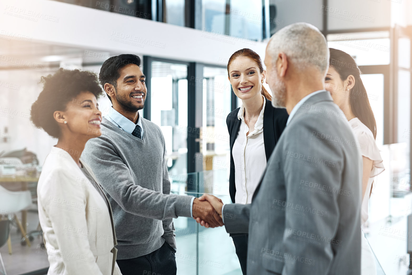 Buy stock photo Shot of two businessmen shaking hands while their colleagues look on