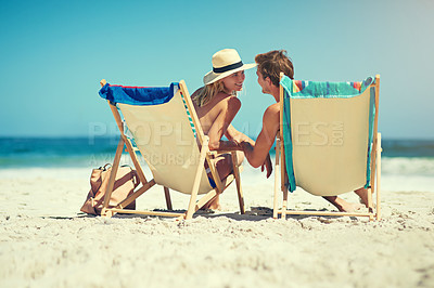 Buy stock photo Rearview shot of a young couple sitting on loungers at the beach