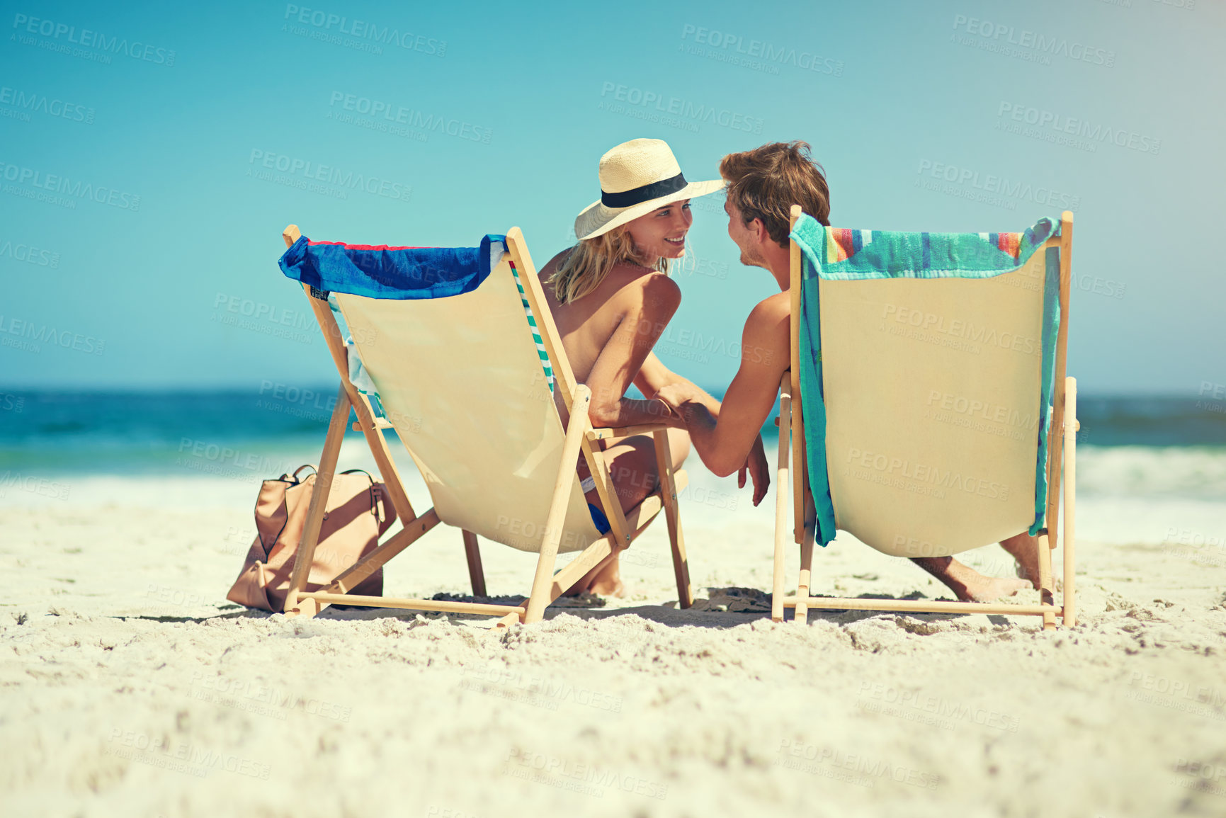 Buy stock photo Rearview shot of a young couple sitting on loungers at the beach