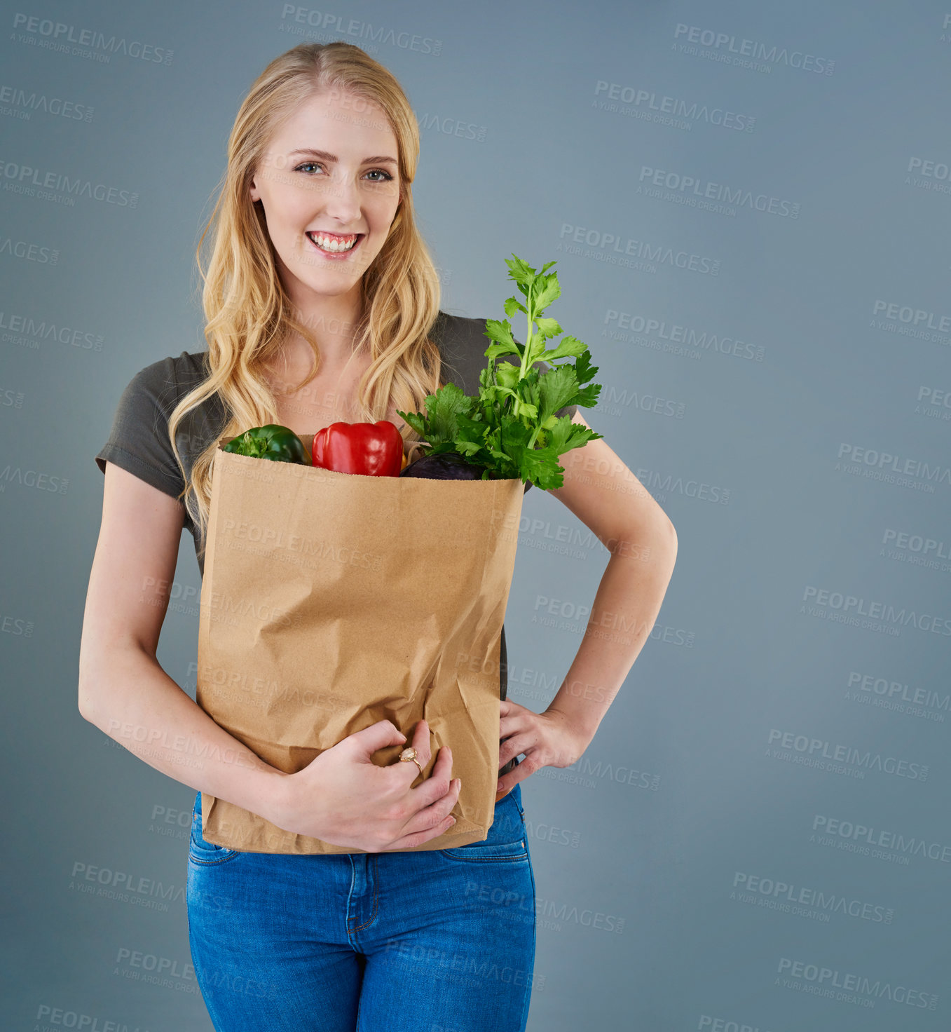 Buy stock photo Cropped studio shot of a young woman holding a paper bag full of vegetables
