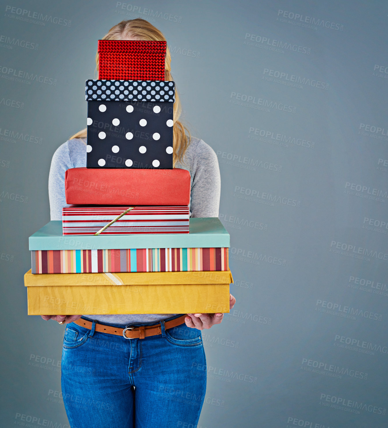 Buy stock photo Cropped studio shot of a young woman holding a stack of presents in front of her face