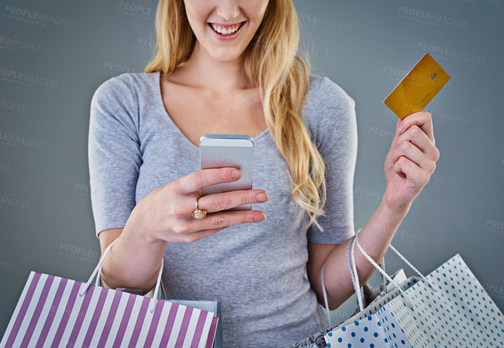 Buy stock photo Cropped studio shot of a young woman holding her smart phone, credit card and shopping bags