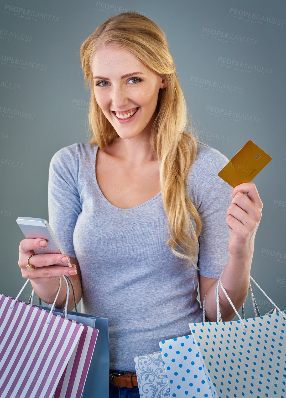 Buy stock photo Cropped studio shot of a young woman holding her smart phone, credit card and shopping bags