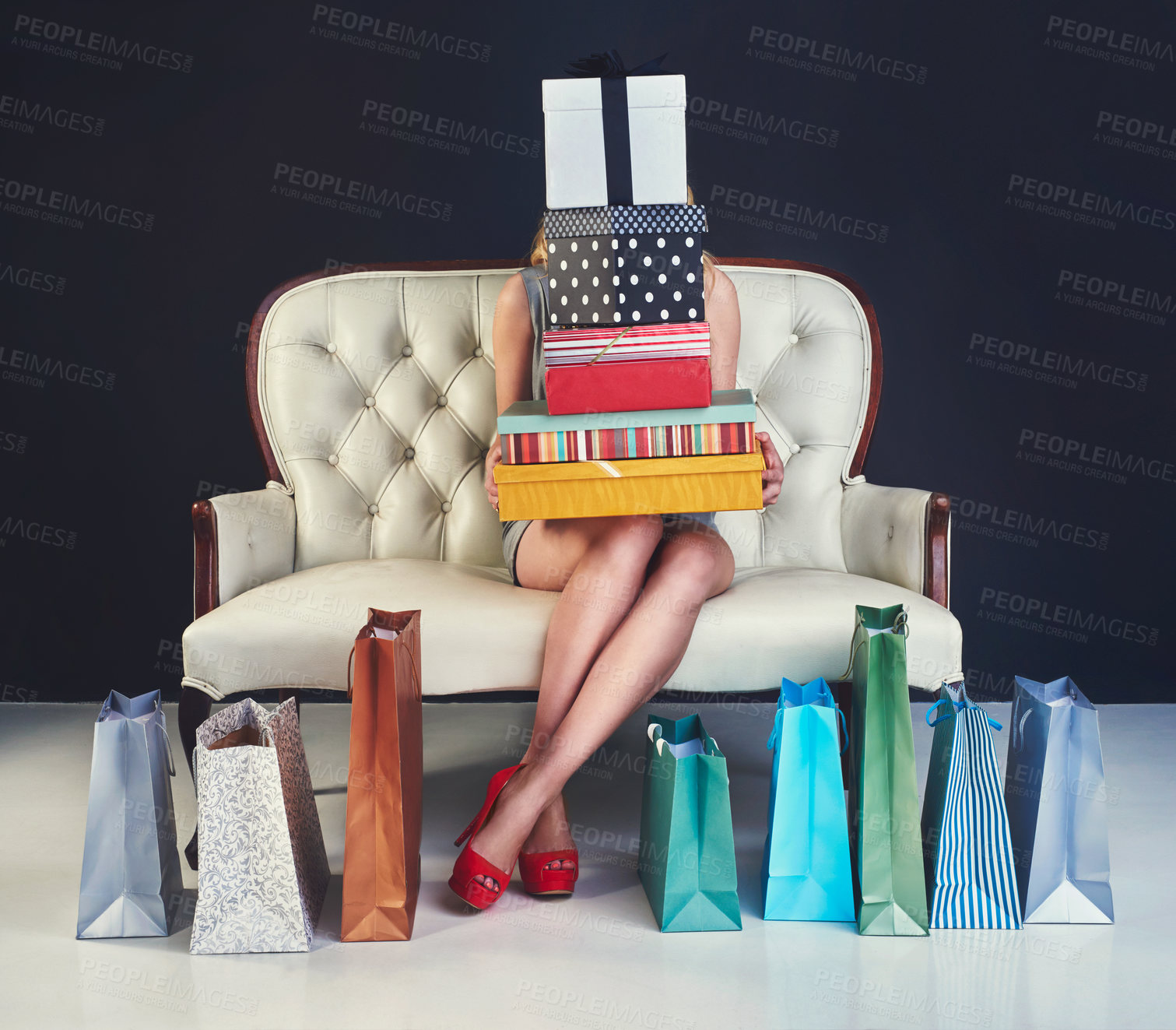 Buy stock photo Studio shot of a young woman sitting on a couch surrounded by gifts