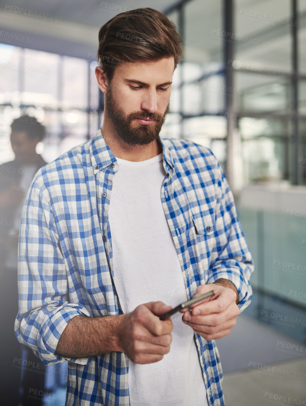 Buy stock photo Cropped shot of a young designer using a cellphone in an office with colleagues in the background