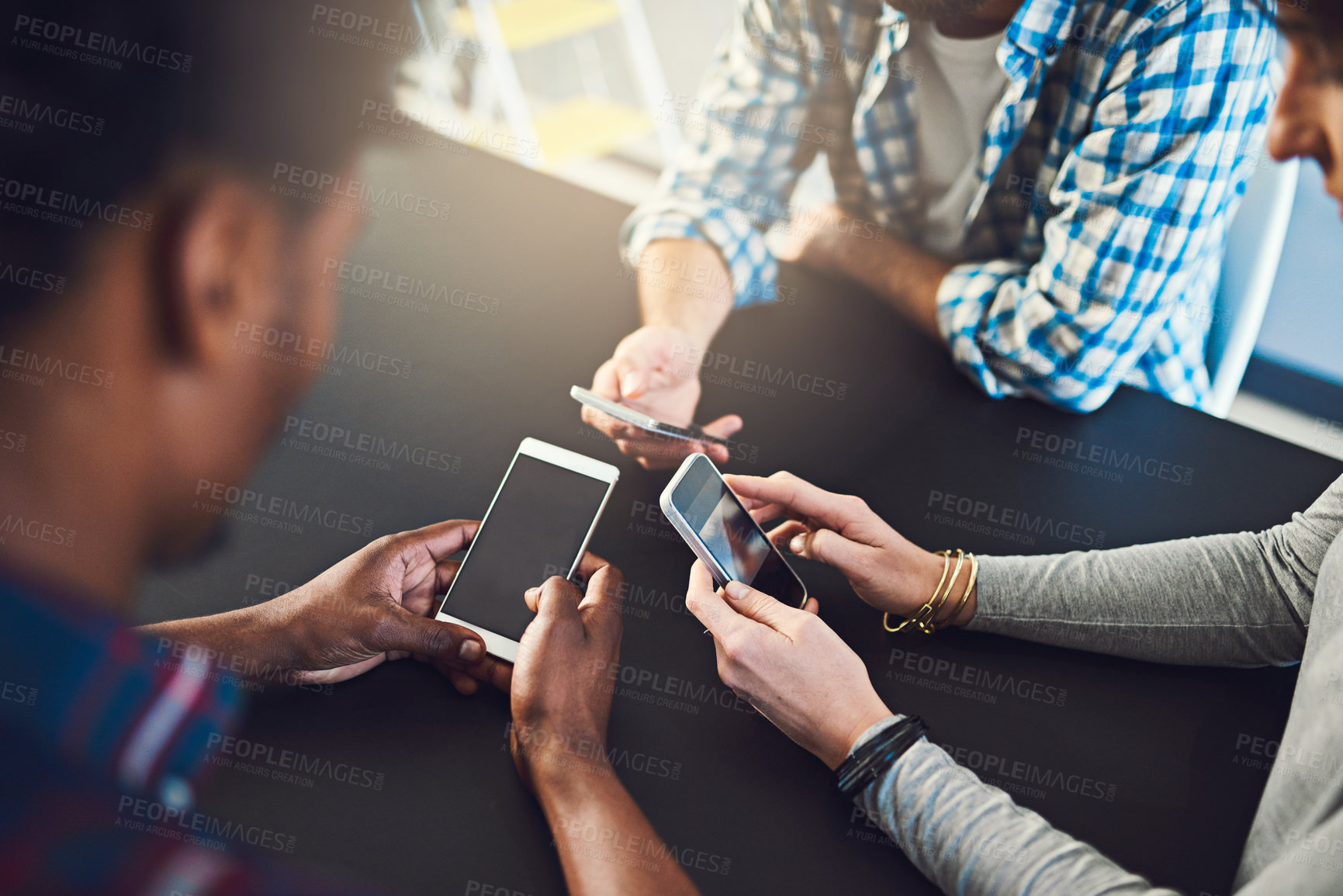 Buy stock photo Cropped shot of three people  sitting around a table together and using their cellphones