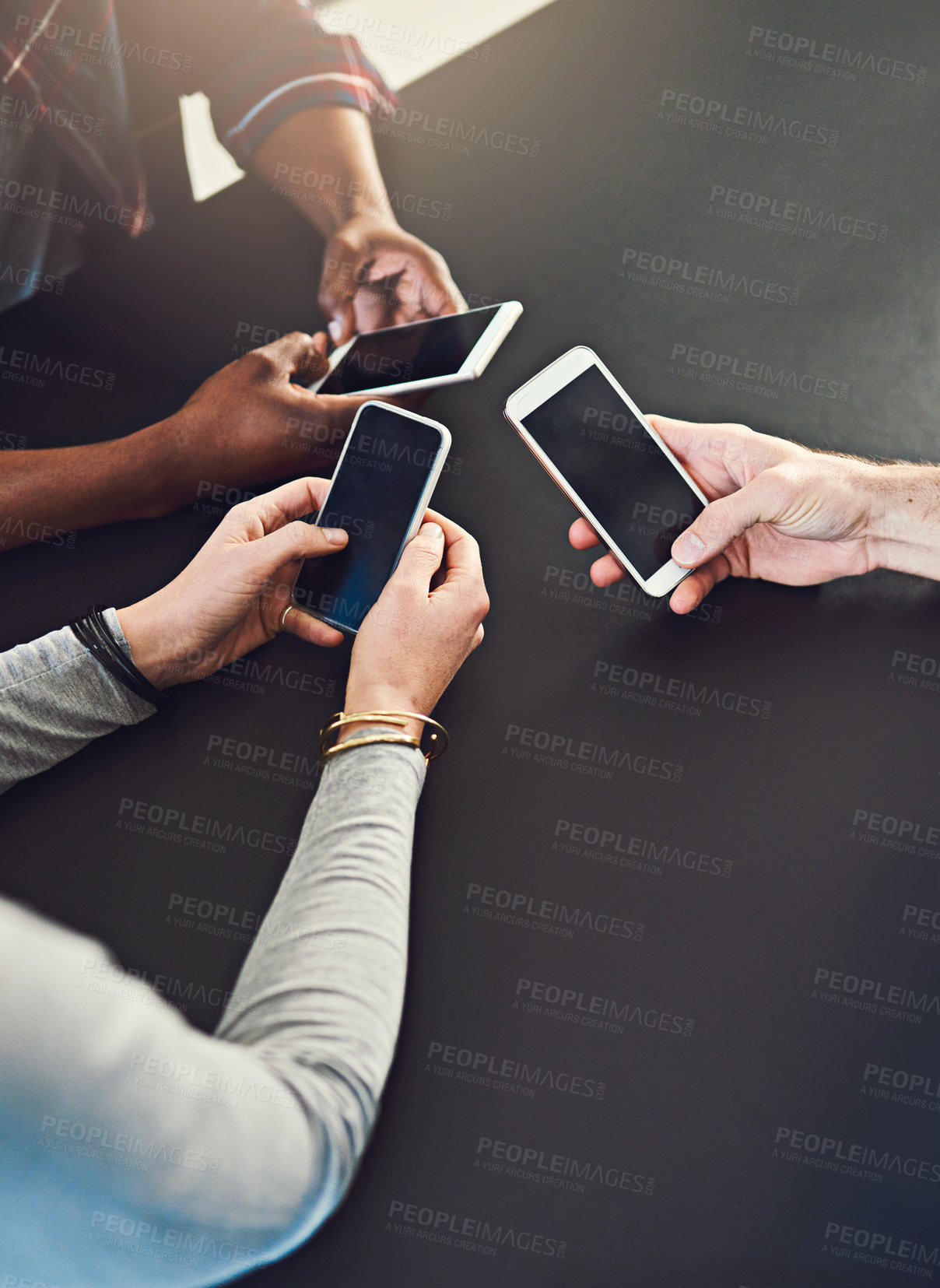 Buy stock photo Cropped shot of three people  sitting around a table together and using their cellphones