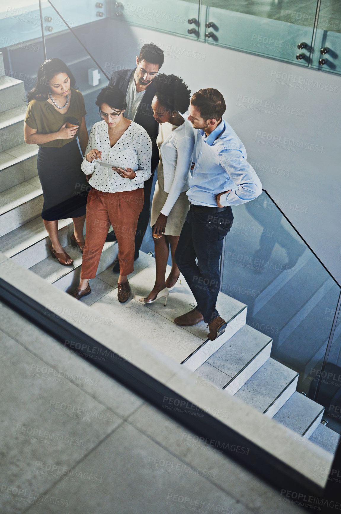 Buy stock photo High angle shot of a group of coworkers looking at a tablet while standing on a staircase in the office