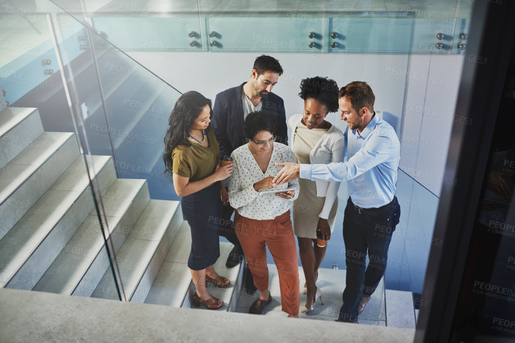 Buy stock photo High angle shot of a group of coworkers looking at a tablet while standing on a staircase in the office