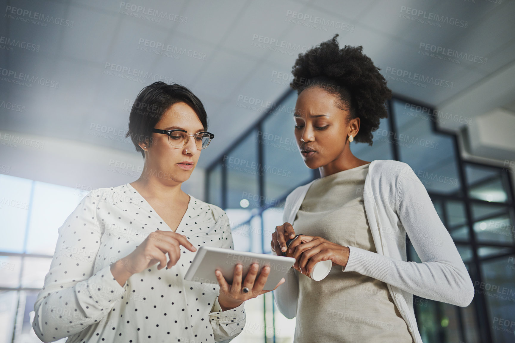 Buy stock photo Low angle shot of two businesswomen looking at a tablet in the office