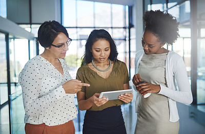 Buy stock photo Cropped shot of three businesswomen looking at a tablet in the office