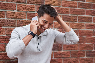 Buy stock photo Cropped shot of a young man speaking on his cellphone outside a brick building