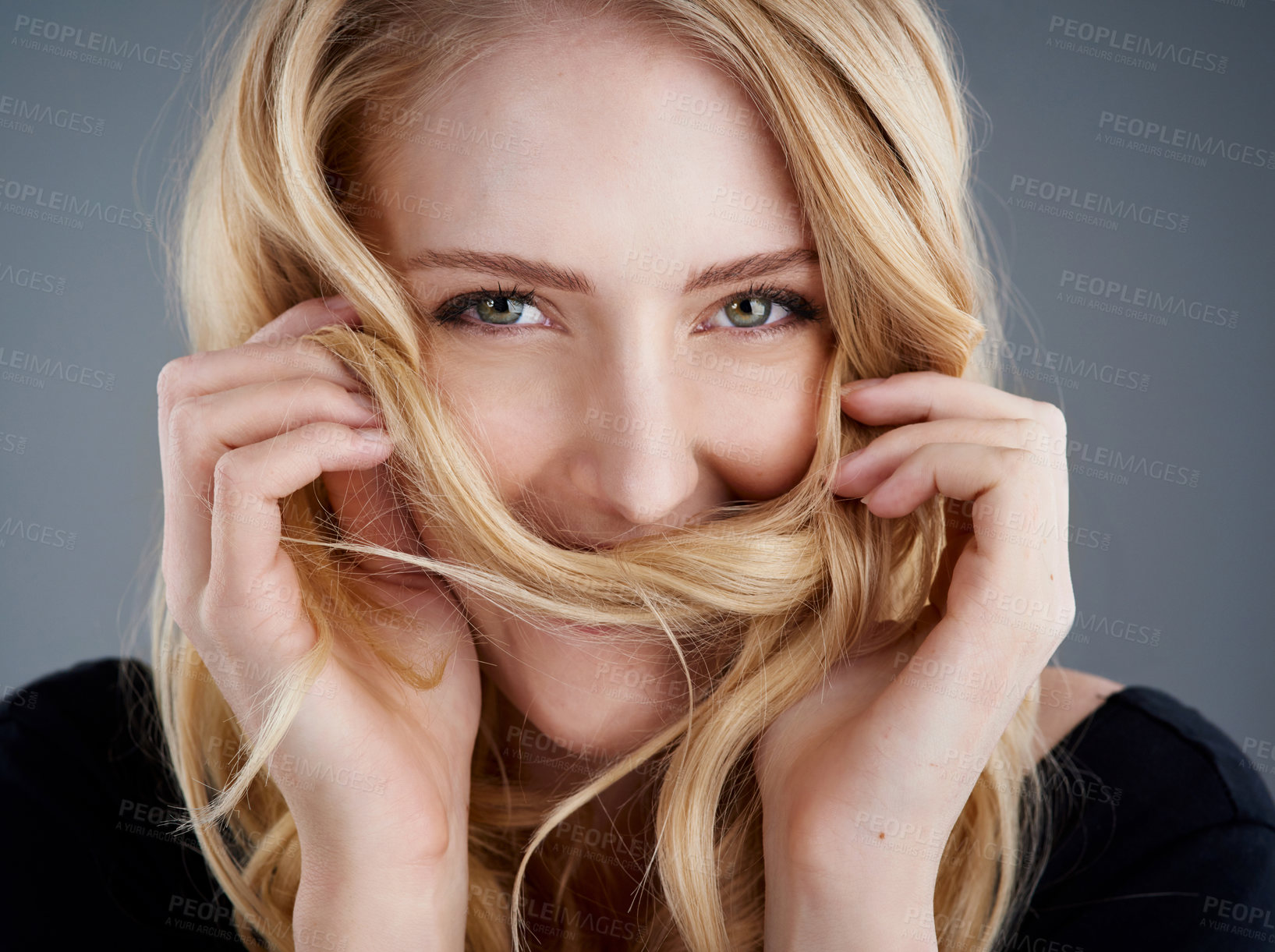 Buy stock photo Studio portrait of an attractive young woman playing with her hair against a gray background