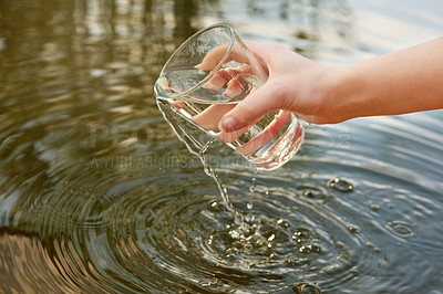 Buy stock photo Cropped shot of water being poured out from a glass into a pond