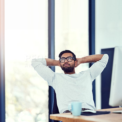 Buy stock photo Cropped shot of a young man sitting at his desk with his hands behind his head
