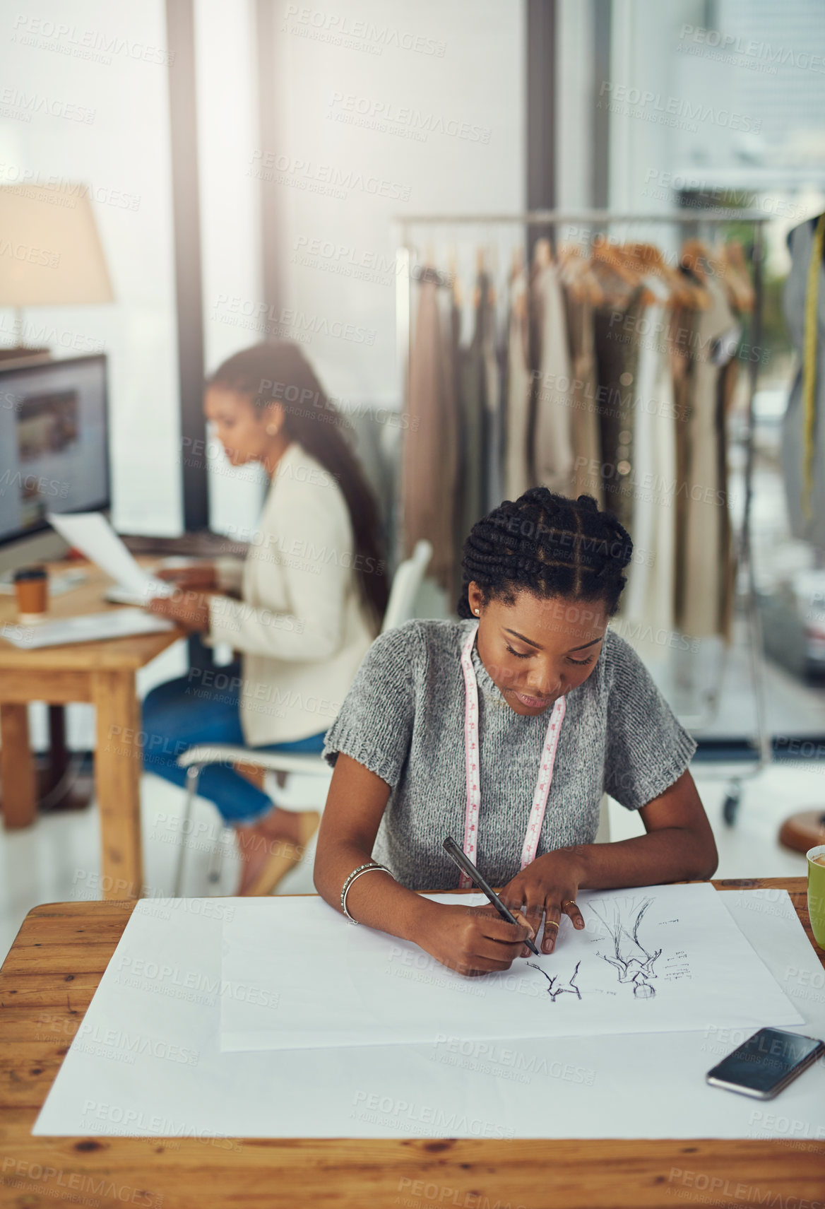 Buy stock photo Shot of a fashion designer working on her latest creation with her colleague blurred out