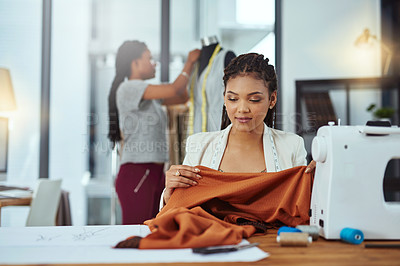 Buy stock photo Shot of a young fashion designer sewing garments while a colleague works on a mannequin in the background