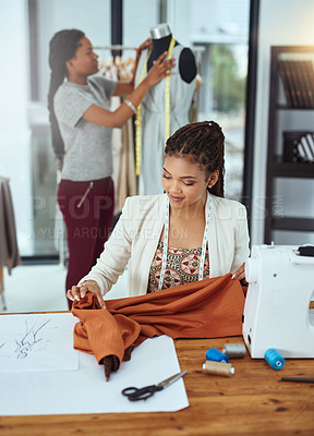 Buy stock photo Shot of a young fashion designer sewing garments while a colleague works on a mannequin in the background