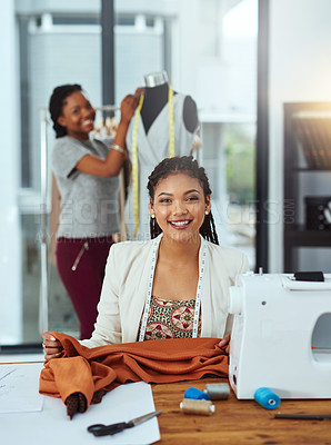 Buy stock photo Portrait of a young fashion designer sewing garments while a colleague works on a mannequin in the background