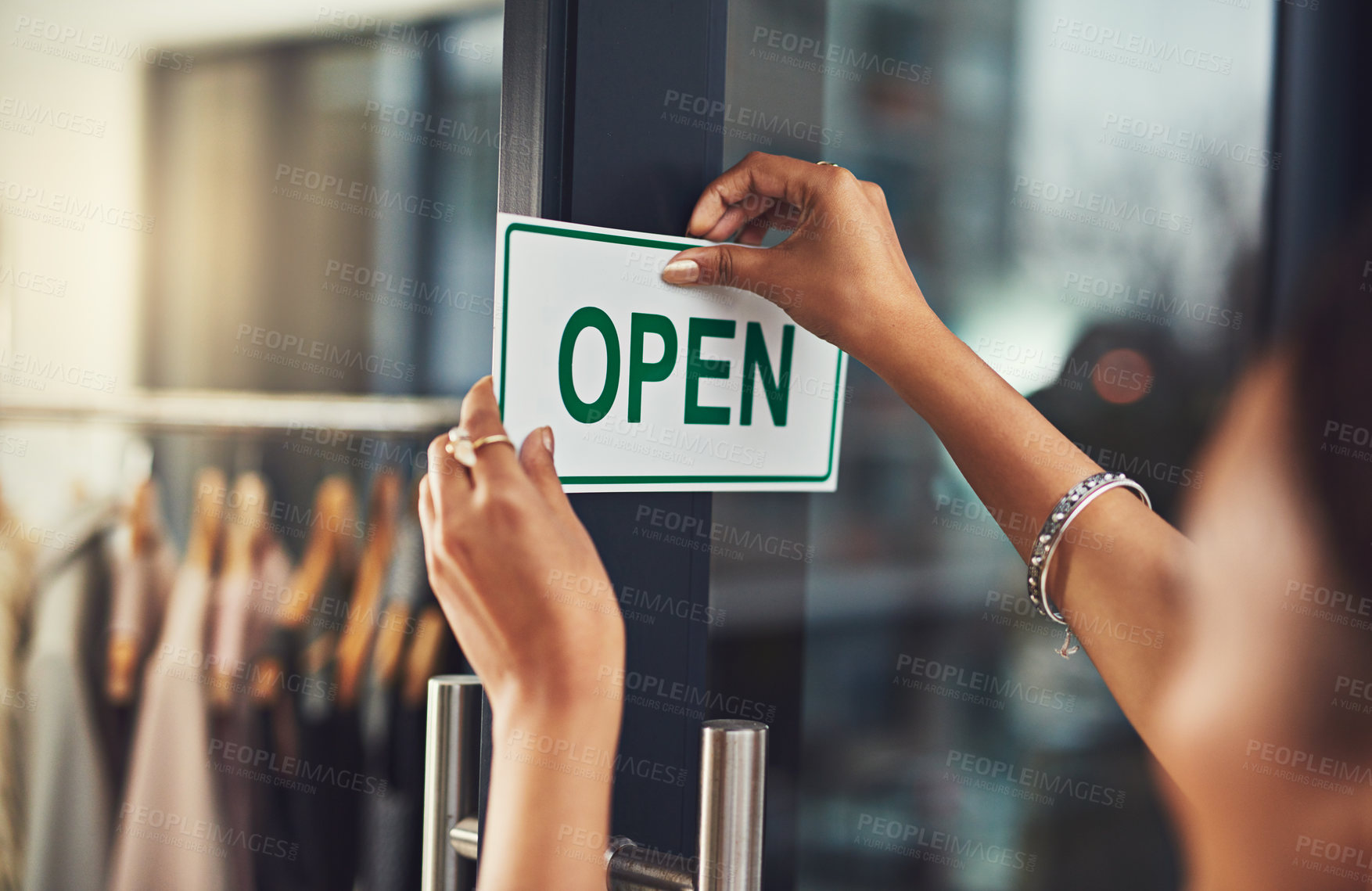 Buy stock photo Closeup shot of a young business owner hanging up an open sign on the door of her shop