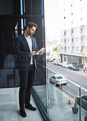 Buy stock photo Shot of a businessman using his tablet while standing on a balcony