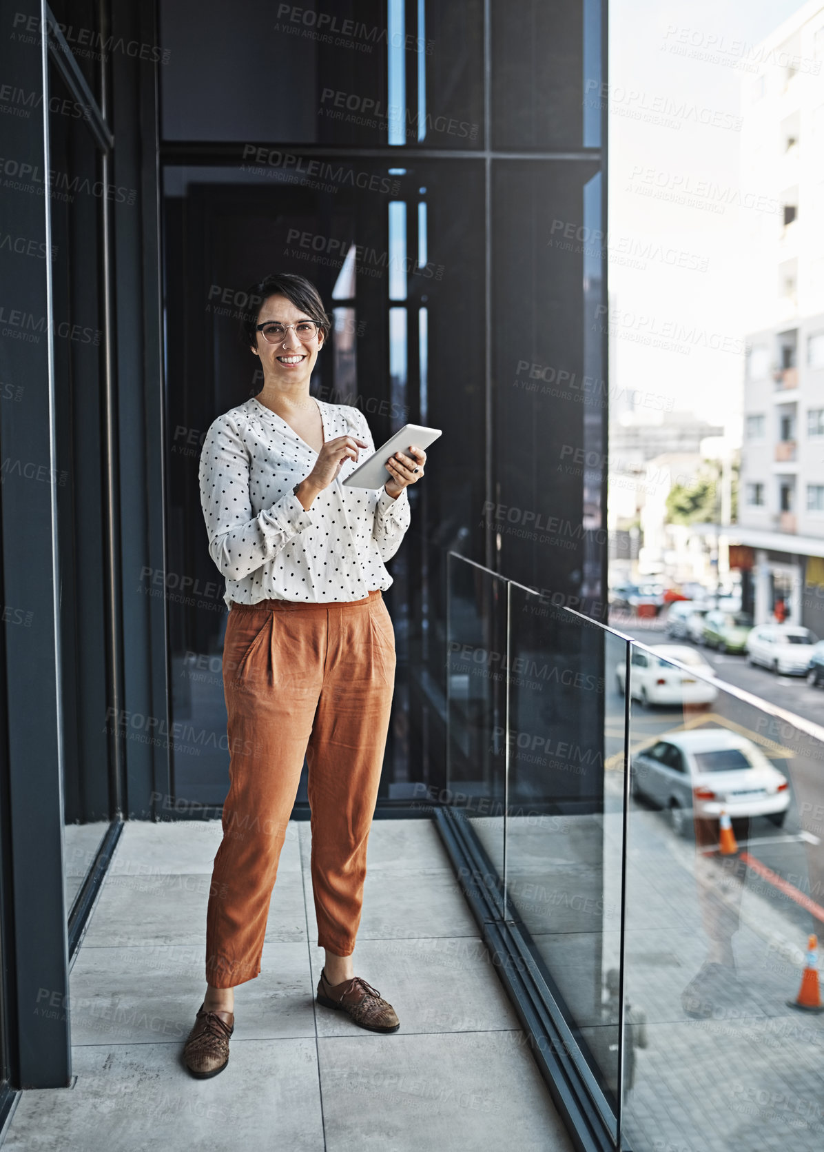 Buy stock photo Shot of a young businesswoman using her tablet while standing on a balcony